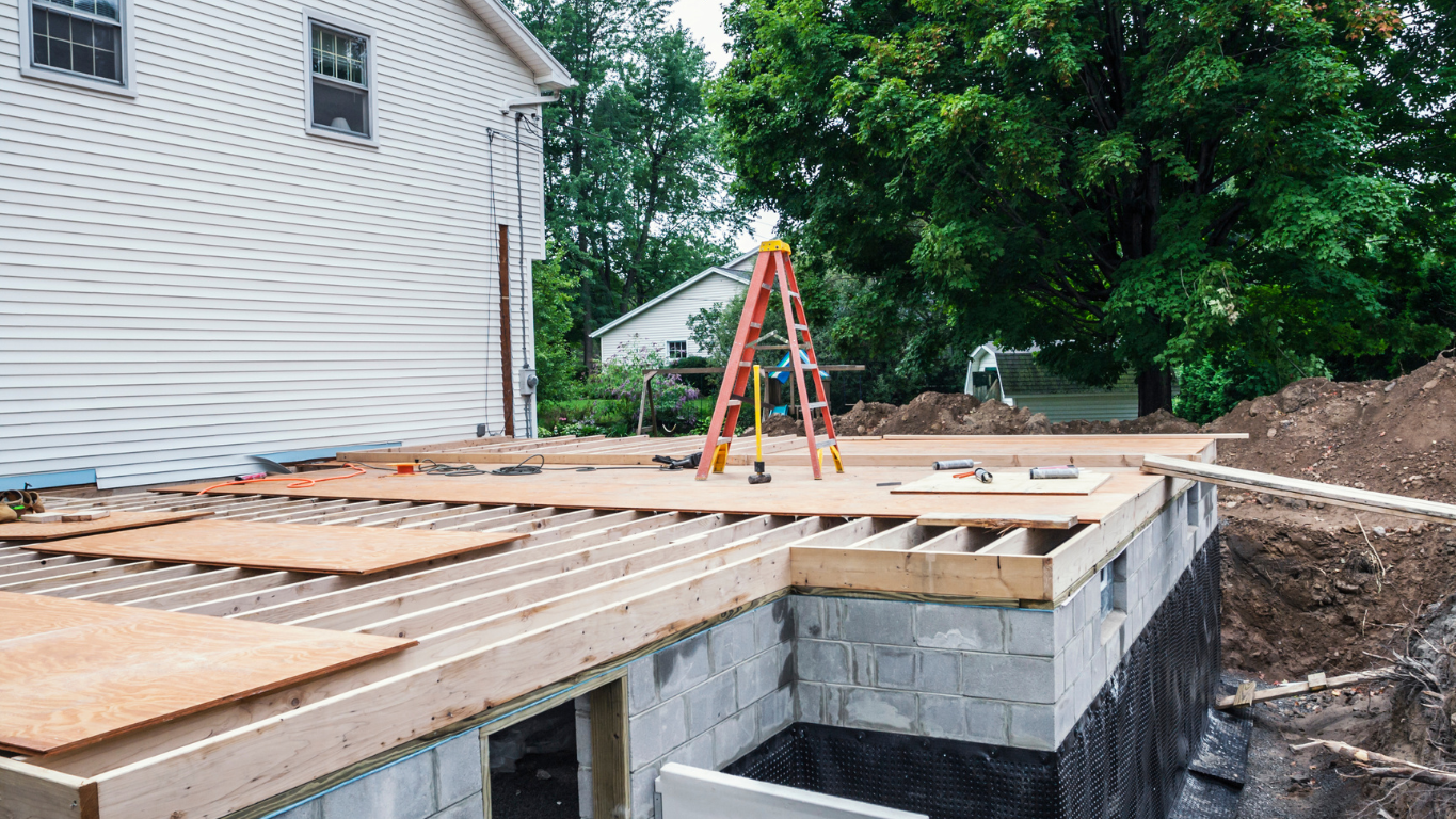 The new foundation and floor joists of a home addition being built onto a house, showing the construction and framing process by a general contractor.