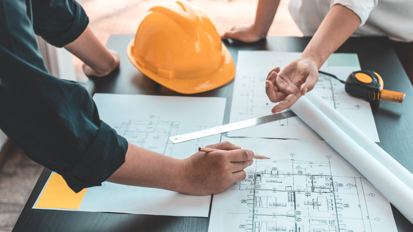 Two contractors or architects reviewing blueprints and engineering plans for a home addition, representing the crucial design and permitting phase.