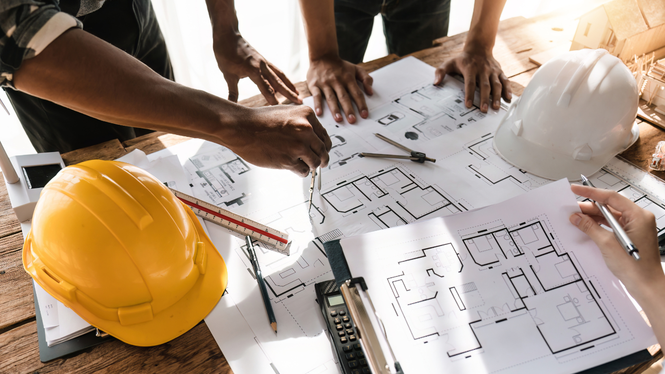A design-build team collaboratively reviewing architectural blueprints on a wooden table with hard hats, symbolizing integrated project planning.
